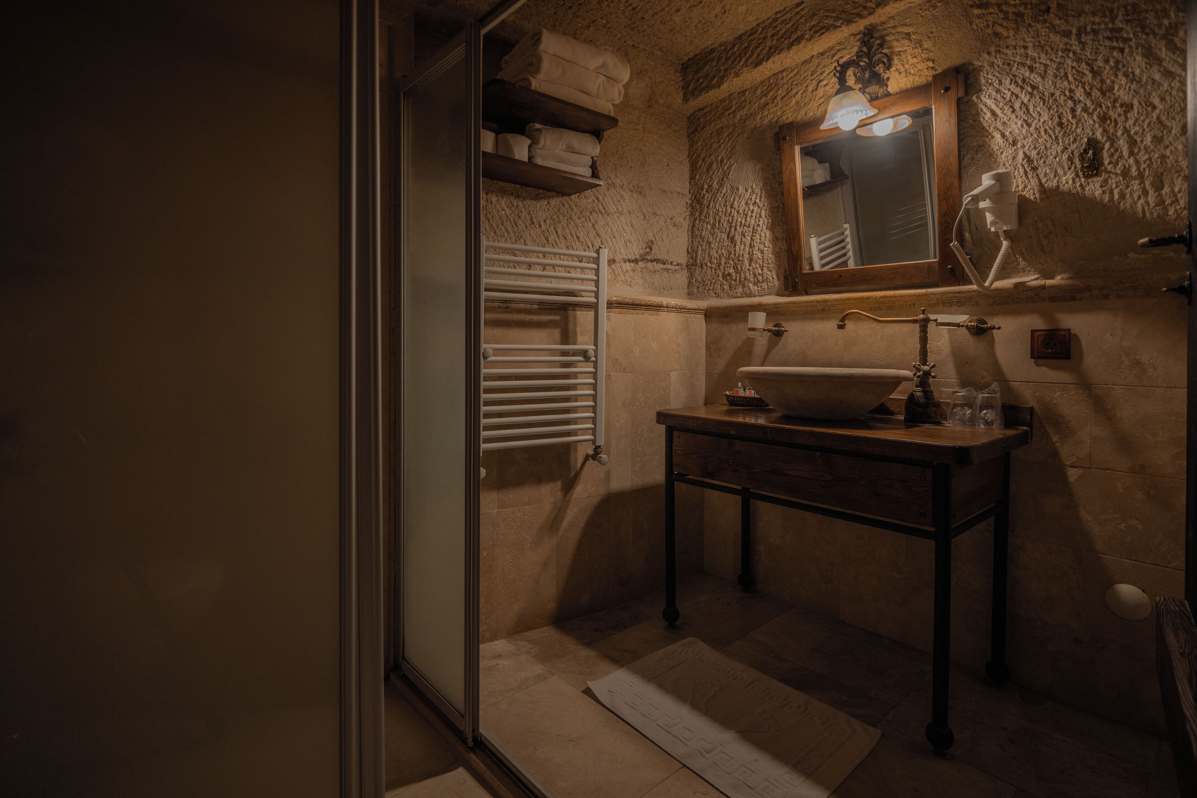 Un baño con pared de piedra, un lavamanos, un espejo y un perchero para toallas.
