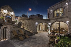 A stone building with arched walkways and a courtyard with wooden furniture and potted plants.