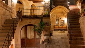 Un intérieur aux murs de pierre, avec une porte en bois, un escalier et un balcon agrémenté de plantes en pot.