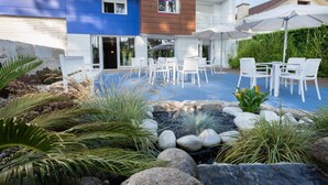 An outdoor patio area with white chairs and tables, a small rock garden, and a building with a blue and brown facade. - Nuevo Norat Sanxenxo (Sanxenxo)