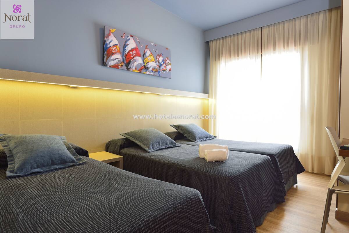 A hotel room with two single beds, a headboard, a painting, and a window with curtains.