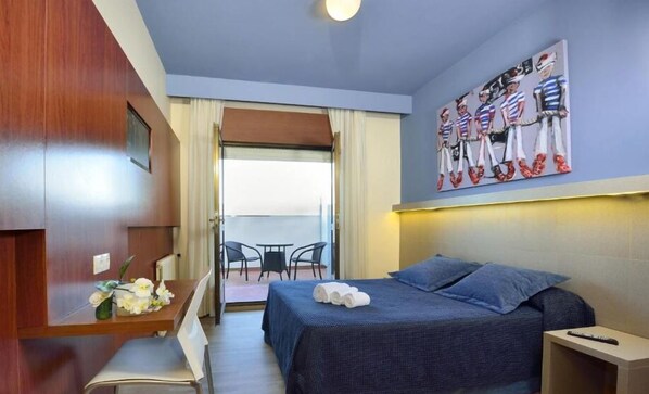 Habitación de hotel con una cama, un escritorio con una silla, una mesita con flores y un cuadro en la pared.