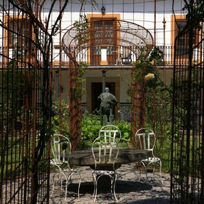 A courtyard with a statue, a table, and chairs, surrounded by a wrought iron fence. - Hotel Quinta Duro (Gijon)