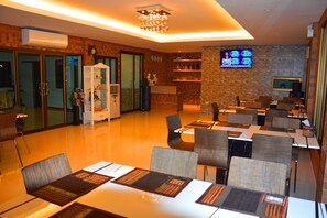 A modern hotel lobby with a dining area, a TV screen, and a decorative plant.