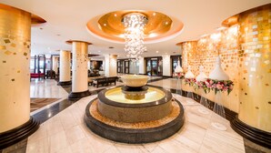 A spacious lobby with a central fountain, high ceilings, and decorative columns.