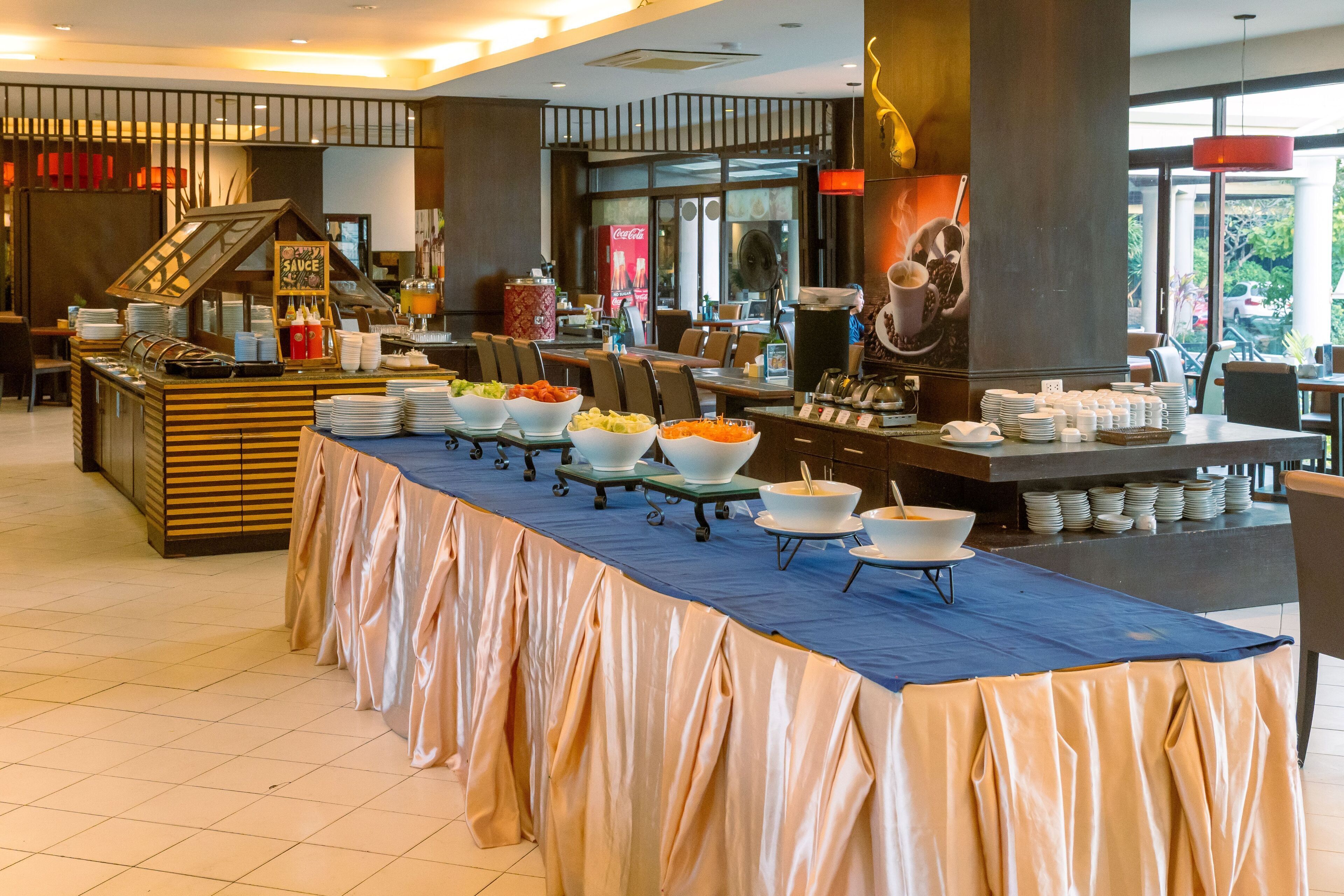 A buffet setup with multiple serving stations, a coffee station, and a Coca-Cola refrigerator.