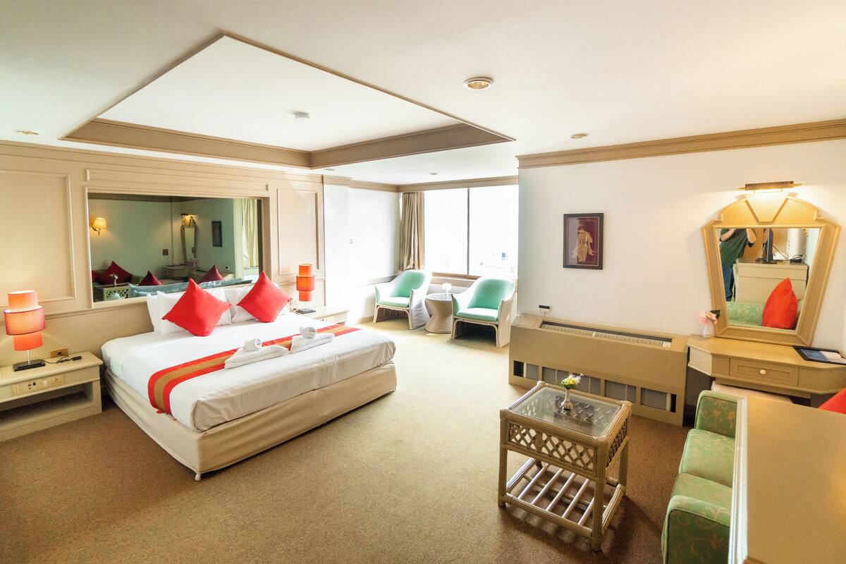 A hotel room with a large bed, a desk, a chair, a small table, and a large window.