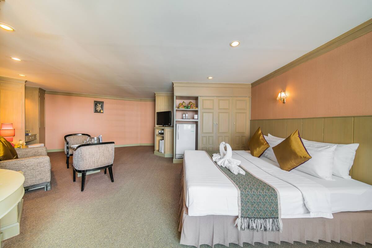 A hotel room with a large bed, two armchairs, a desk, a minibar, and a television.