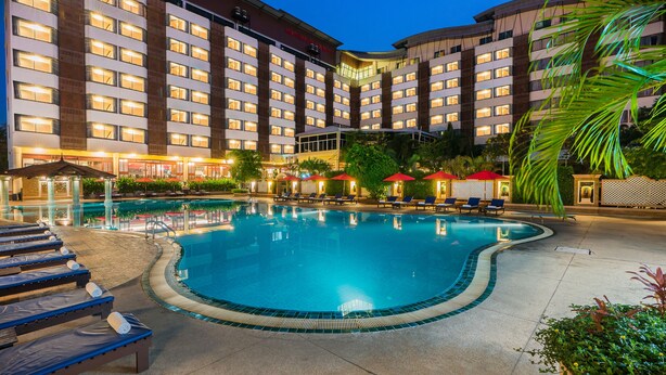 A hotel with a swimming pool, sun loungers, and a covered area with umbrellas.
