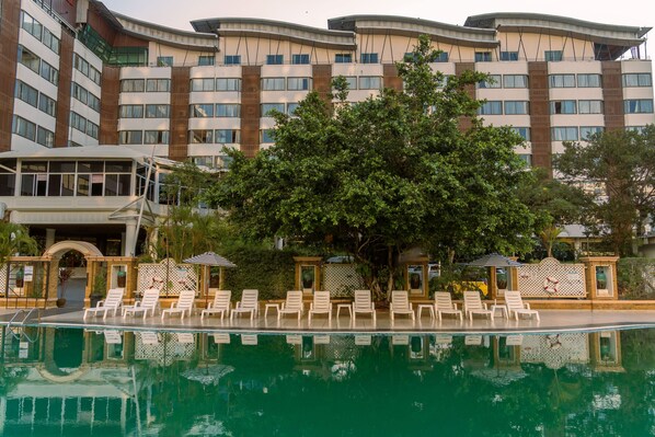 A hotel with a swimming pool, lounge chairs, and a large tree in front. - Mountain Beach Resort (Pattaya)