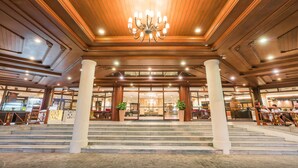 A grand lobby with a chandelier, large columns, and a staircase leading to the entrance.