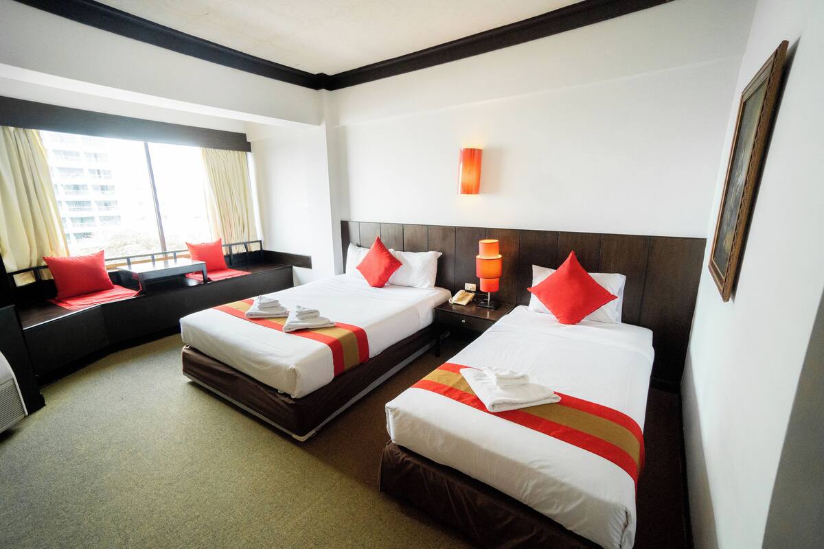 A hotel room with two beds, a window with curtains, a bedside table, and a wall-mounted lamp.