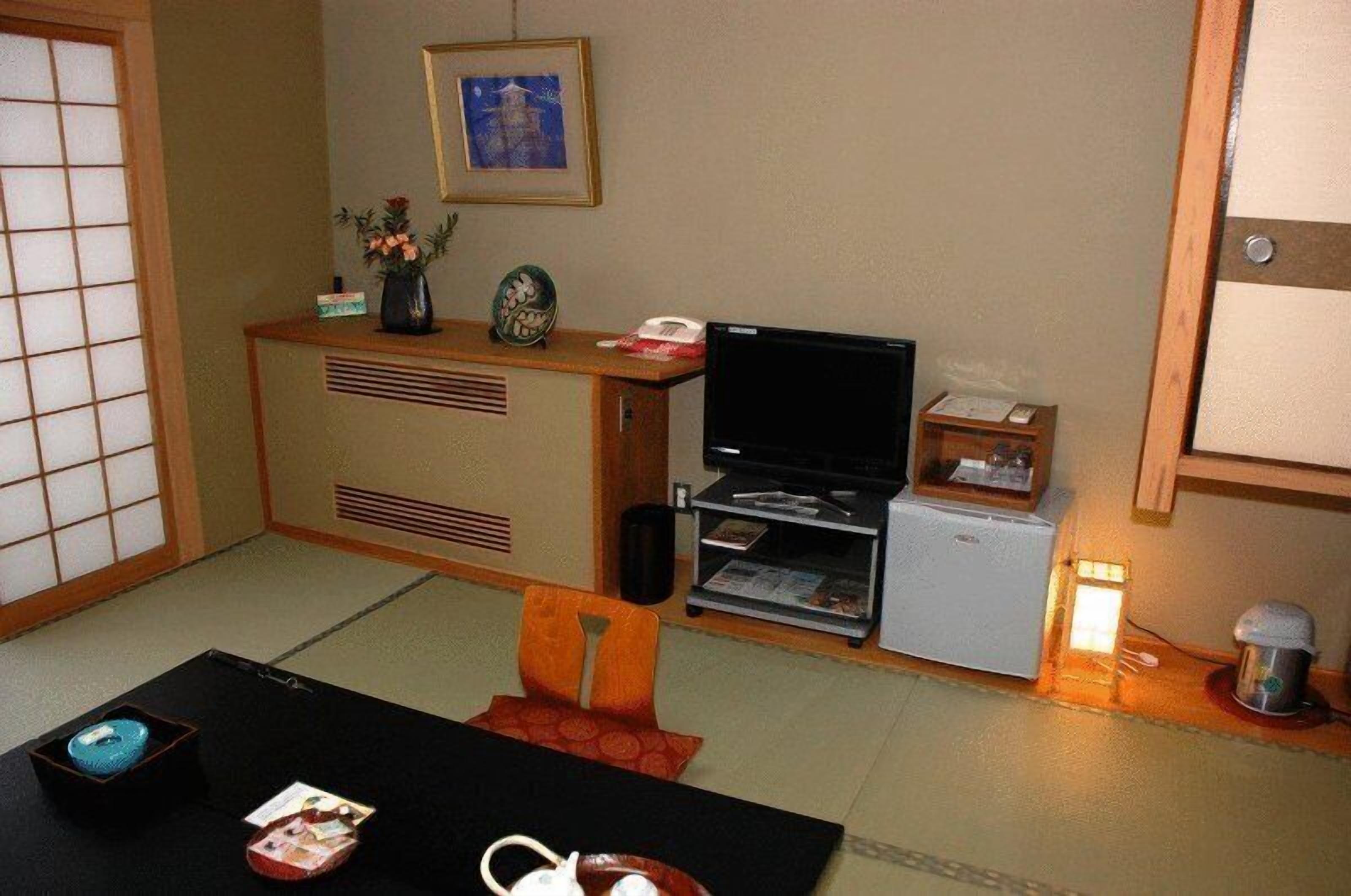 A traditional Japanese-style room with tatami flooring, a low wooden table, a television, and a small refrigerator.