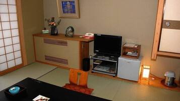 A traditional Japanese-style room with tatami flooring, a low wooden table, a television, and a small refrigerator.