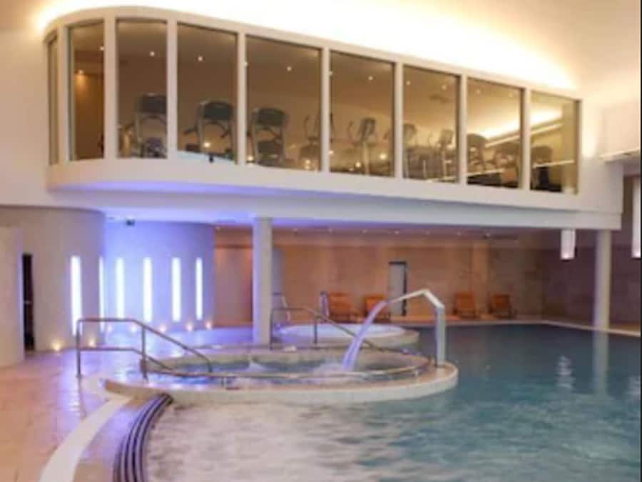 An indoor swimming pool with a sunken hot tub, a glass-enclosed upper deck, and a tiled floor.