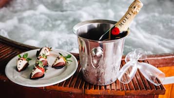 A metal bucket with a champagne bottle, ice cubes, and a plate with food items on a wooden surface.