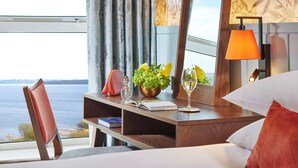 A hotel room with a view of the sea, a desk with a book, a glass of wine, and a lamp. - Hodson Bay Hotel (Athlone)