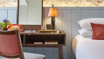 A hotel room with a wooden desk, a telephone, a lamp, and a bed with white and red pillows.