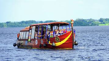A boat with a red and yellow design, a covered upper deck, and passengers visible.
