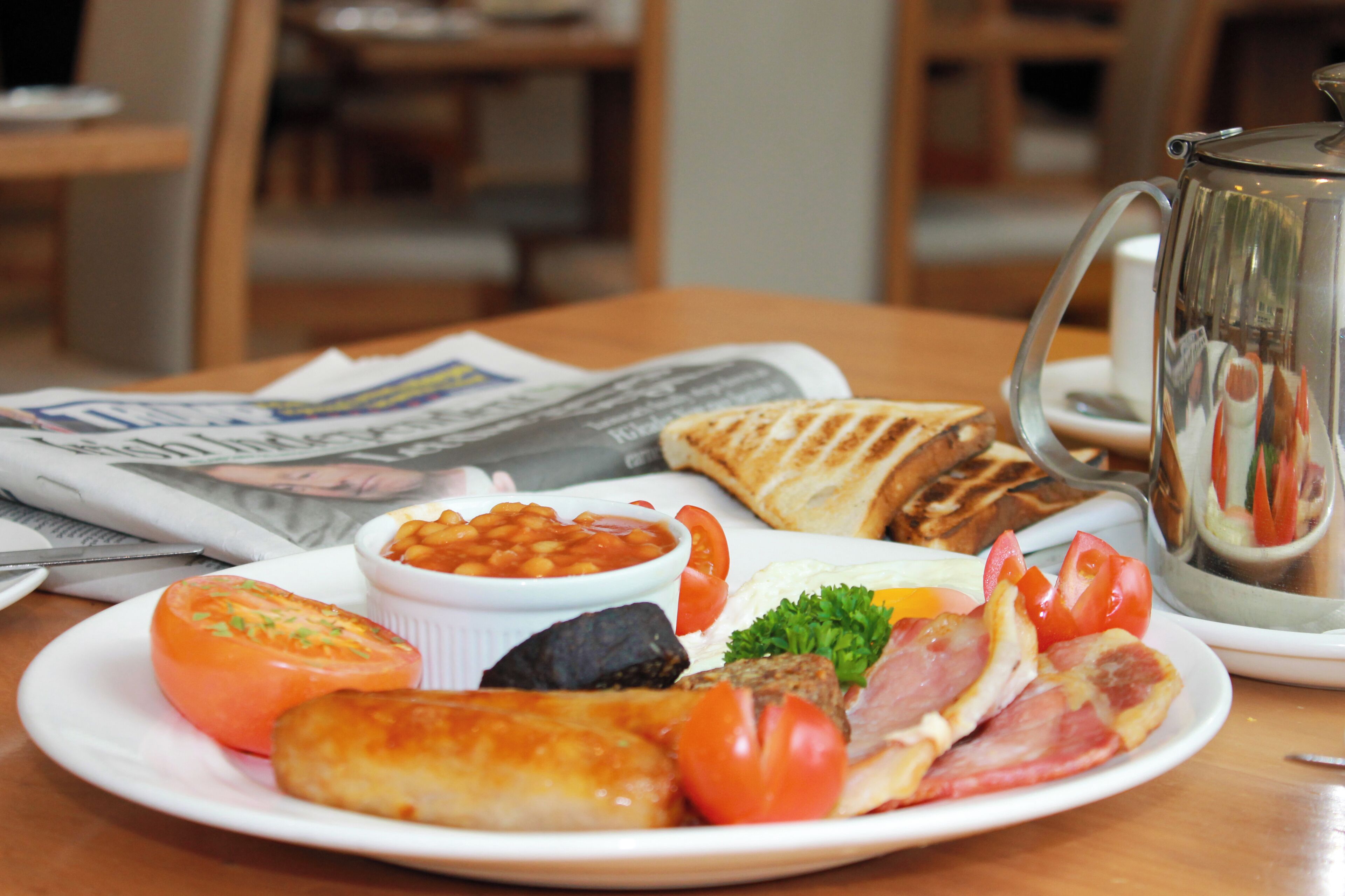 A breakfast plate with eggs, bacon, tomatoes, beans, and toast on a wooden table.