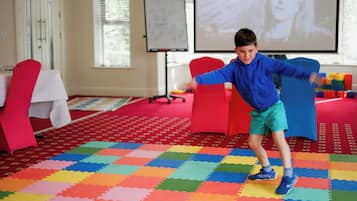 A child playing on a colorful foam mat in a room with a red carpet, a whiteboard, and a projector screen.