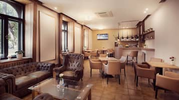 A spacious lounge area with leather sofas, a glass coffee table, and a bar area with shelves and a television.
