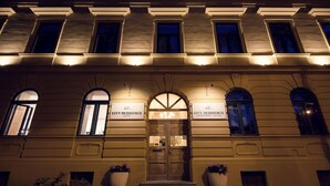 Un bâtiment doté d’une grande entrée en arc de cercle, avec deux plantes en pot de chaque côté, et des panneaux indiquant « City Residence Cafe » et « City Residence Apartment Hotel ».
