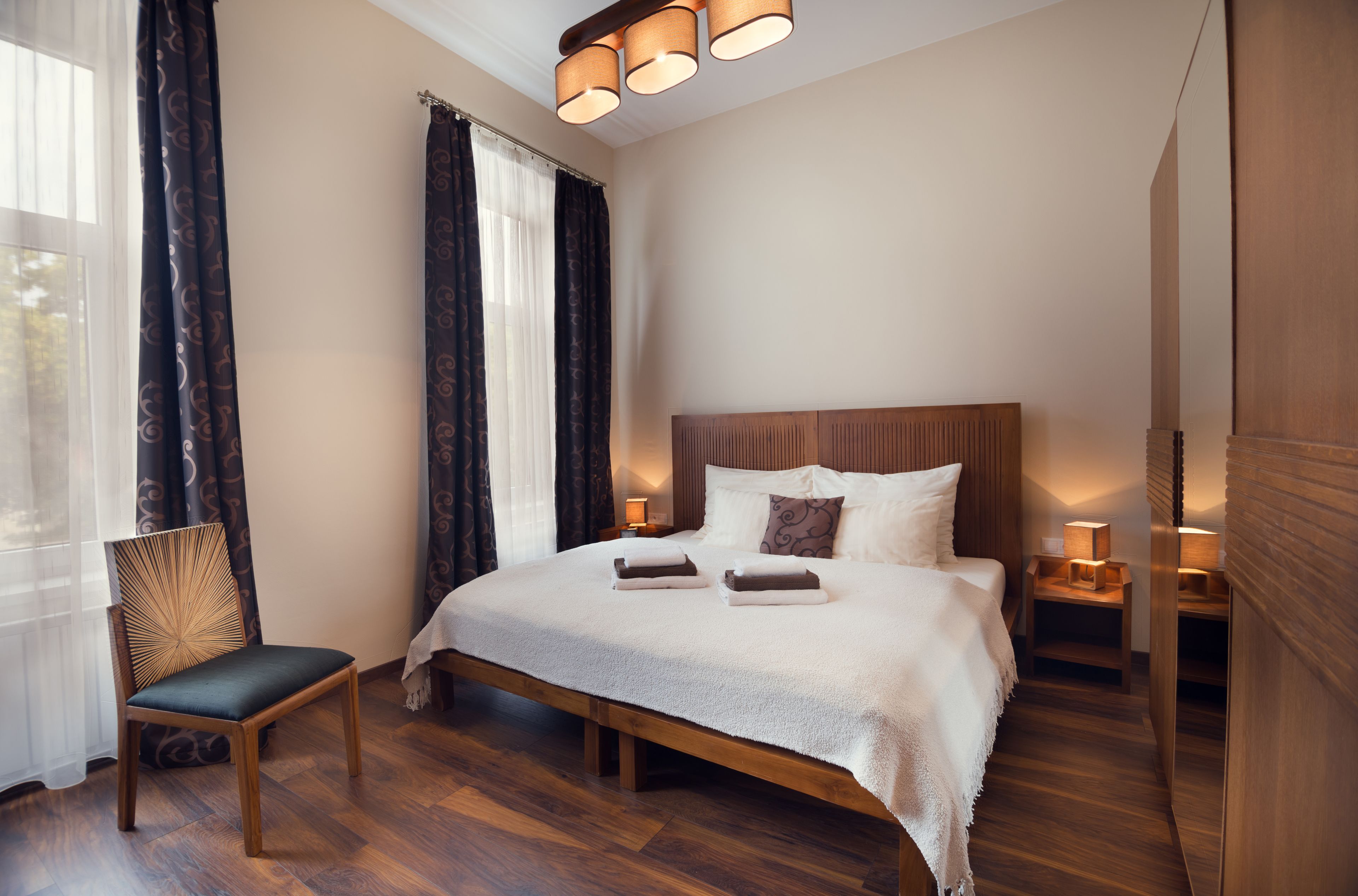 Ein ordentlich eingerichtetes Schlafzimmer mit einem großen Bett, einem hölzernen Stuhl und einem Nachttisch mit Lampe.