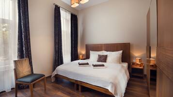 Un dormitorio ordenado con una cama grande, una silla de madera y una mesita de noche con una lámpara.