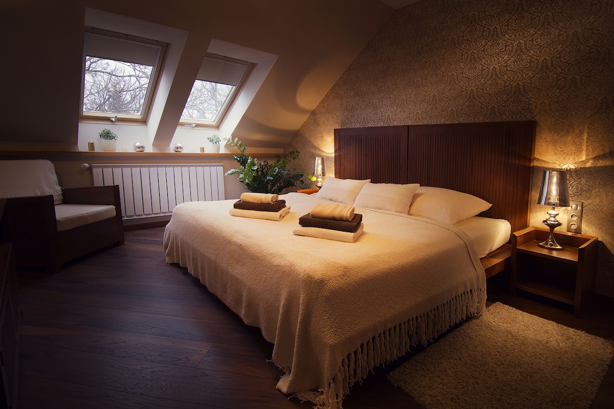 A bedroom with a large bed, two bedside tables, a nightstand, a window, and a radiator.