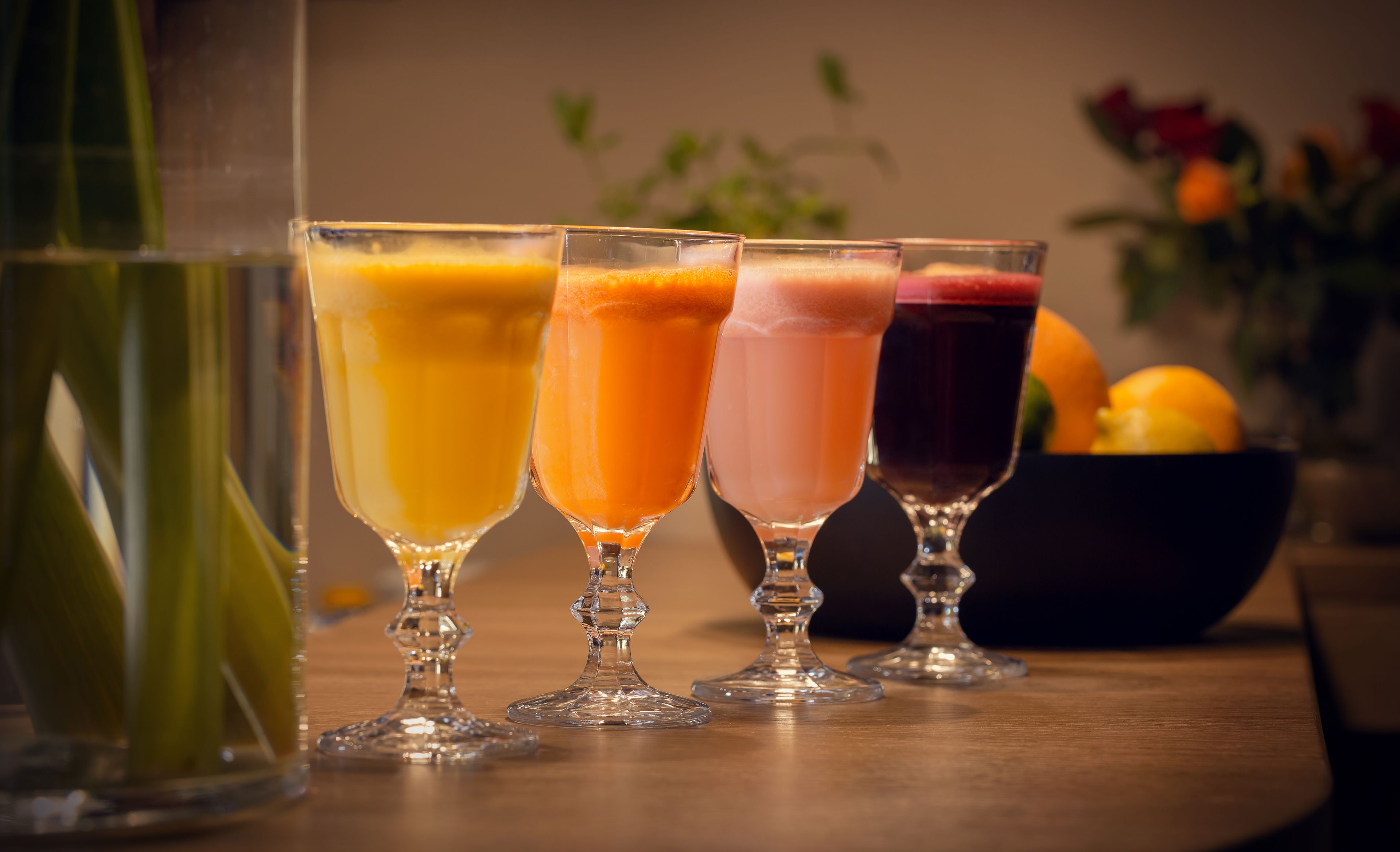 Four glasses of different colored beverages on a wooden table.