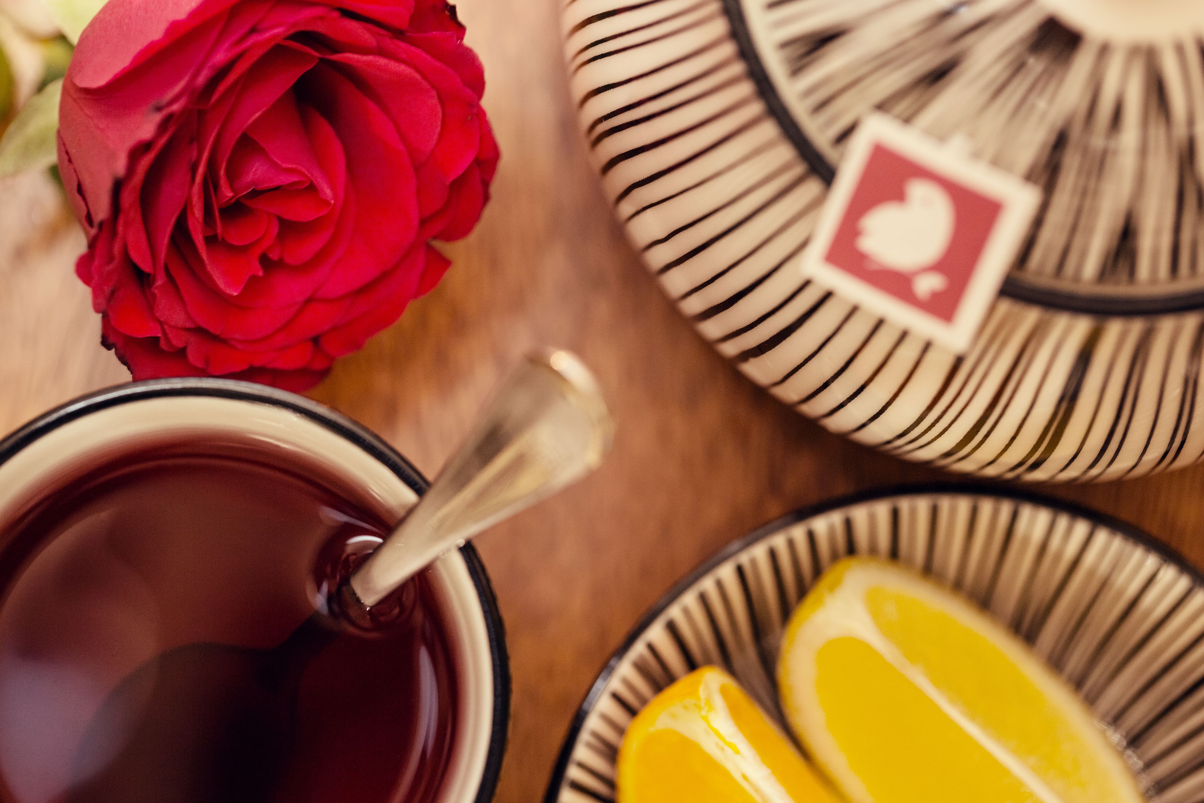 Un primer plano de una rosa roja, un vaso de líquido rojo con una cuchara y un plato con rodajas de limón.