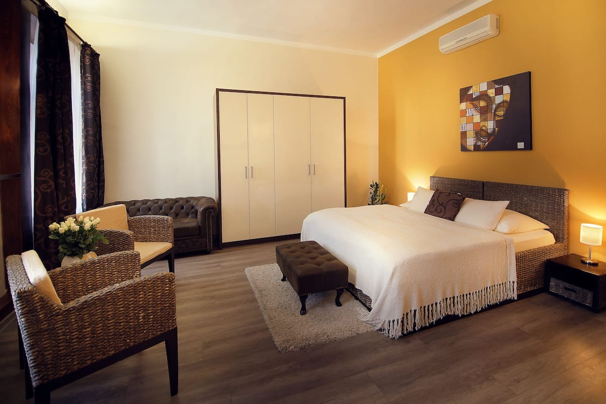 A hotel room with a bed, a chair, a small table, a nightstand, and a wardrobe.