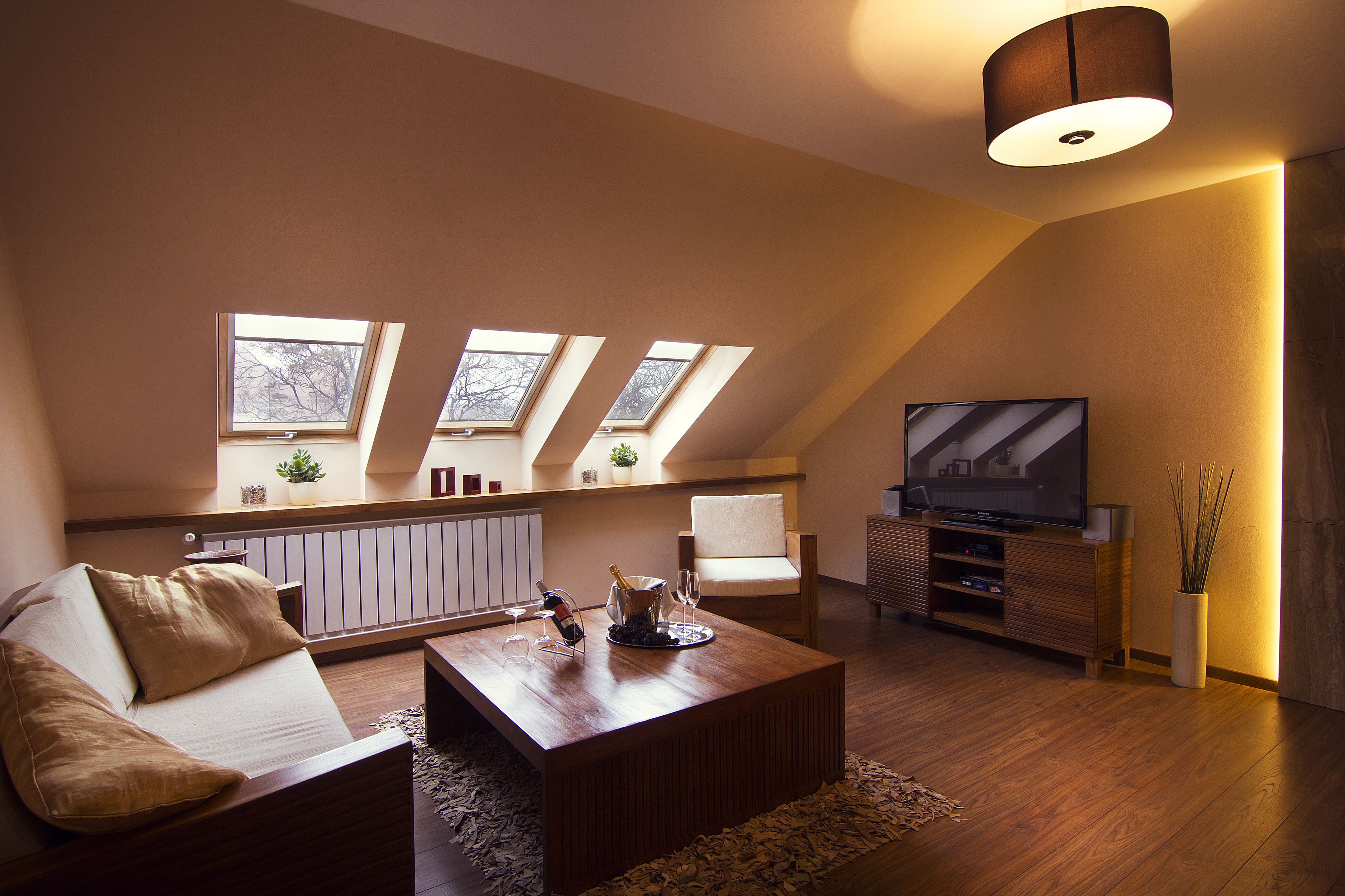 Una sala de estar moderna con un sofá, una mesa de centro y un televisor. Hay tragaluces, una planta y un mueble con un televisor.