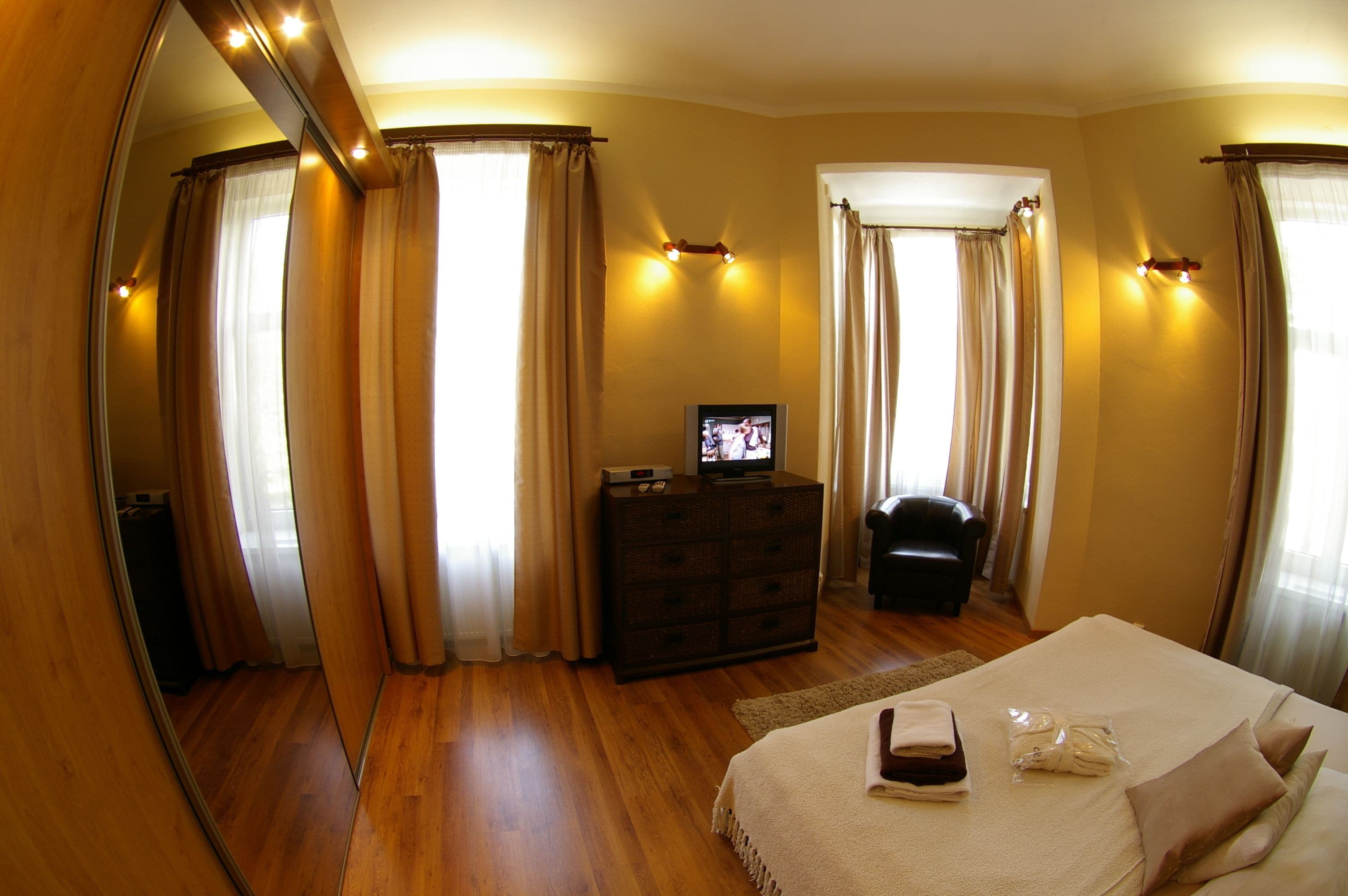 Una habitación de hotel con una cama grande, un aparador, un televisor y cortinas.