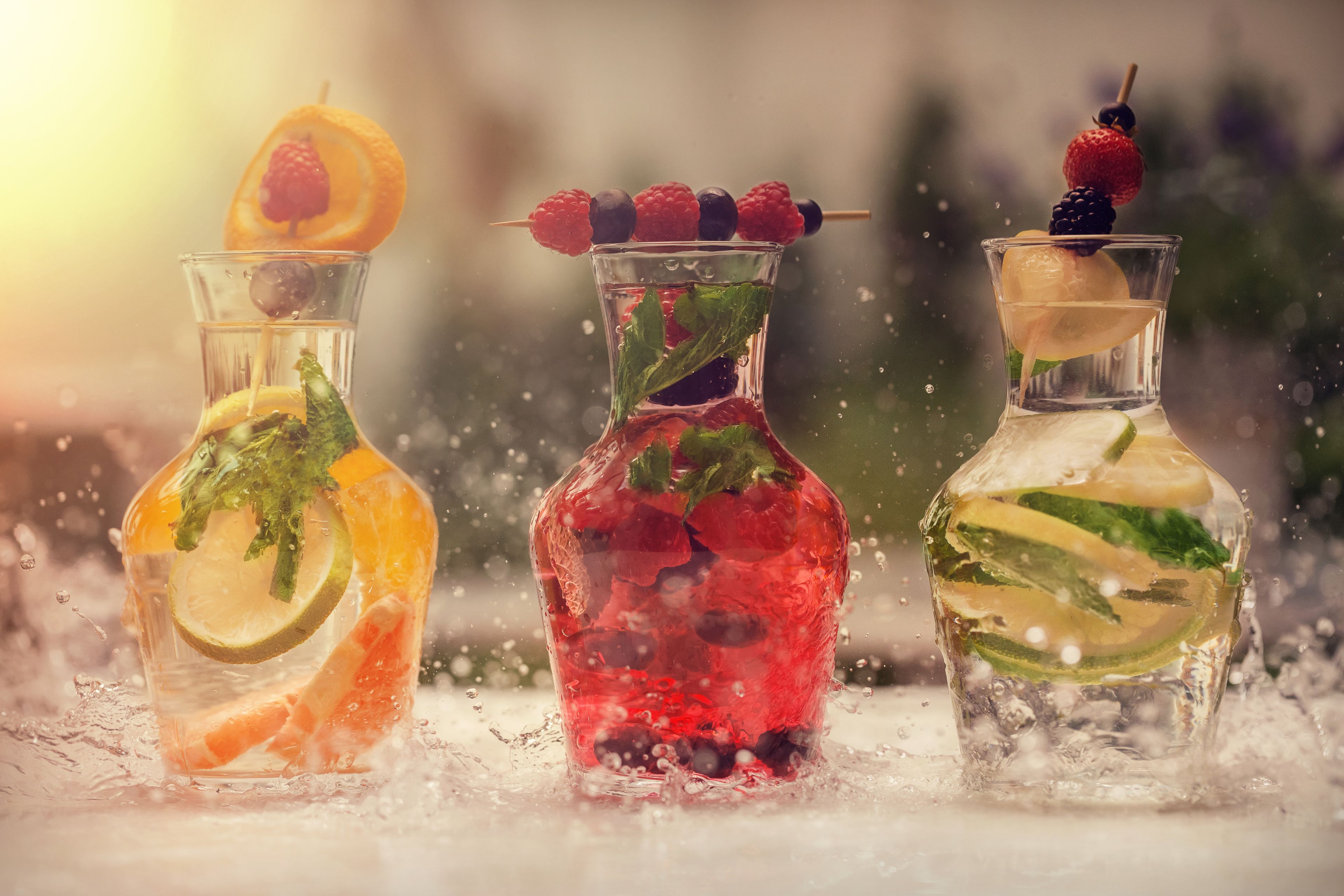 Three glass bottles with different colored liquids and garnishes, each containing various fruits and herbs.