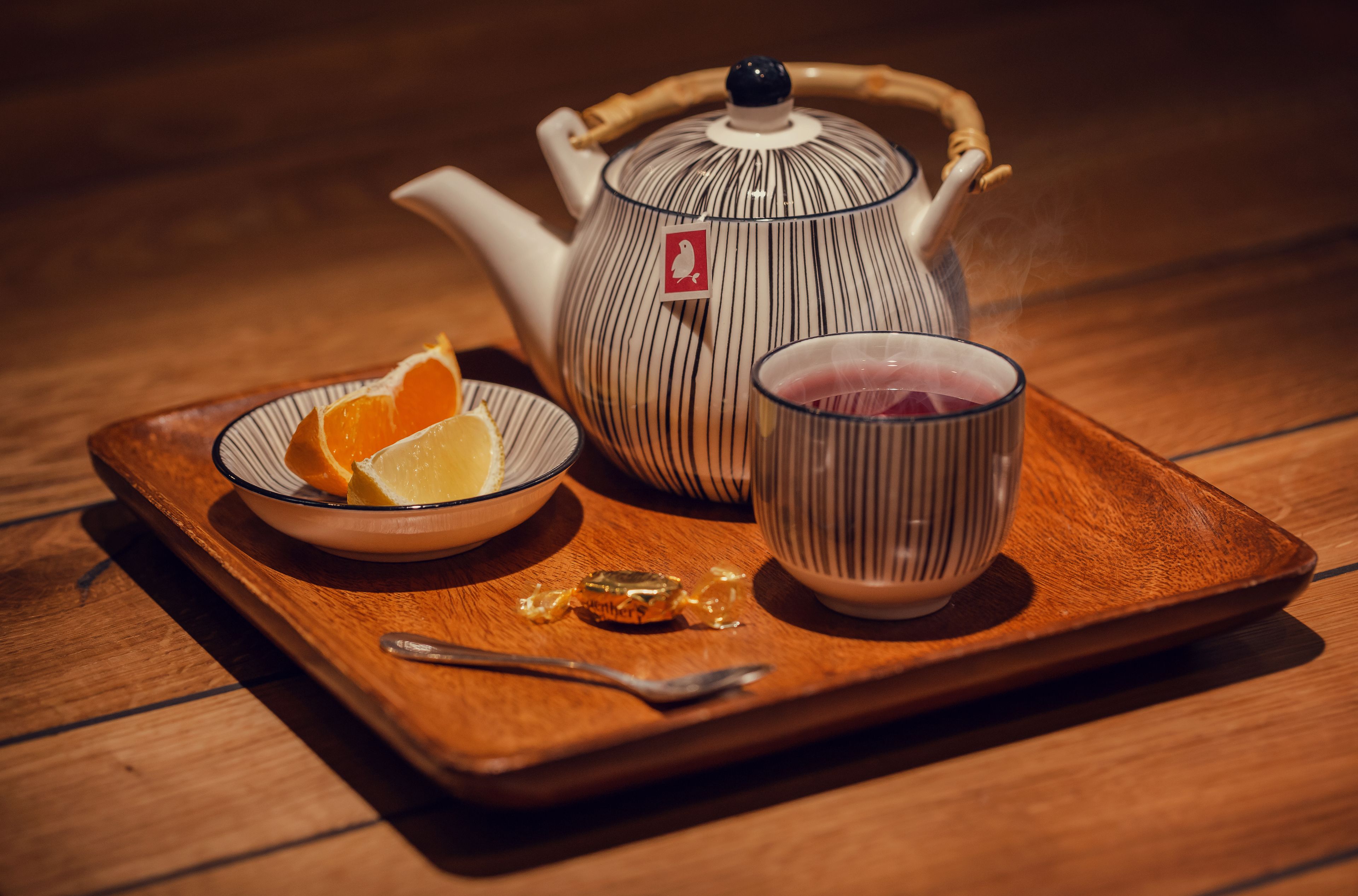 Une théière, une tasse et un bol contenant des tranches d’orange, le tout posé sur un plateau en bois.