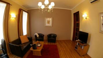 Ein Wohnzimmer mit einer Couch, zwei Sesseln, einem Couchtisch, einem Fernseher auf einem Holzboden und einer Kristallleuchtre.