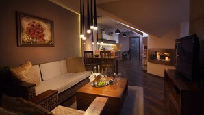 Un salon moderne avec un canapé, une table basse sur laquelle se trouve une bouteille de champagne et des verres, un téléviseur et une cheminée.