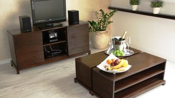 A living room with a dark wooden entertainment center, a flat-screen TV, a speaker, a potted plant, a fruit tray, and a champagne bucket.