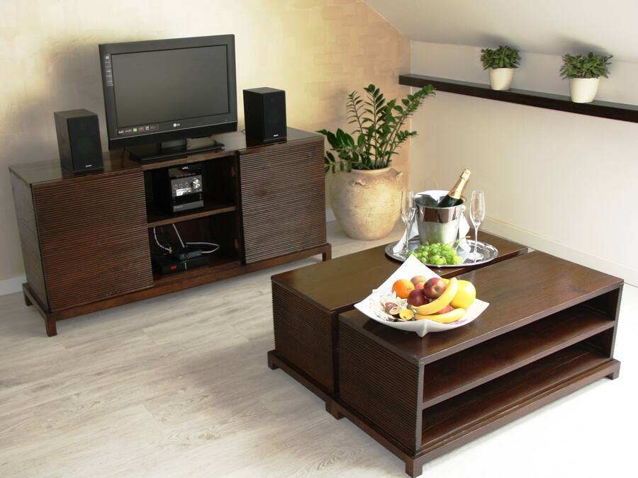 A living room with a dark wooden entertainment center, a flat-screen TV, a speaker, a potted plant, a fruit tray, and a champagne bucket.