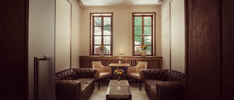A room with a sofa set, a coffee table, and two windows with potted plants.