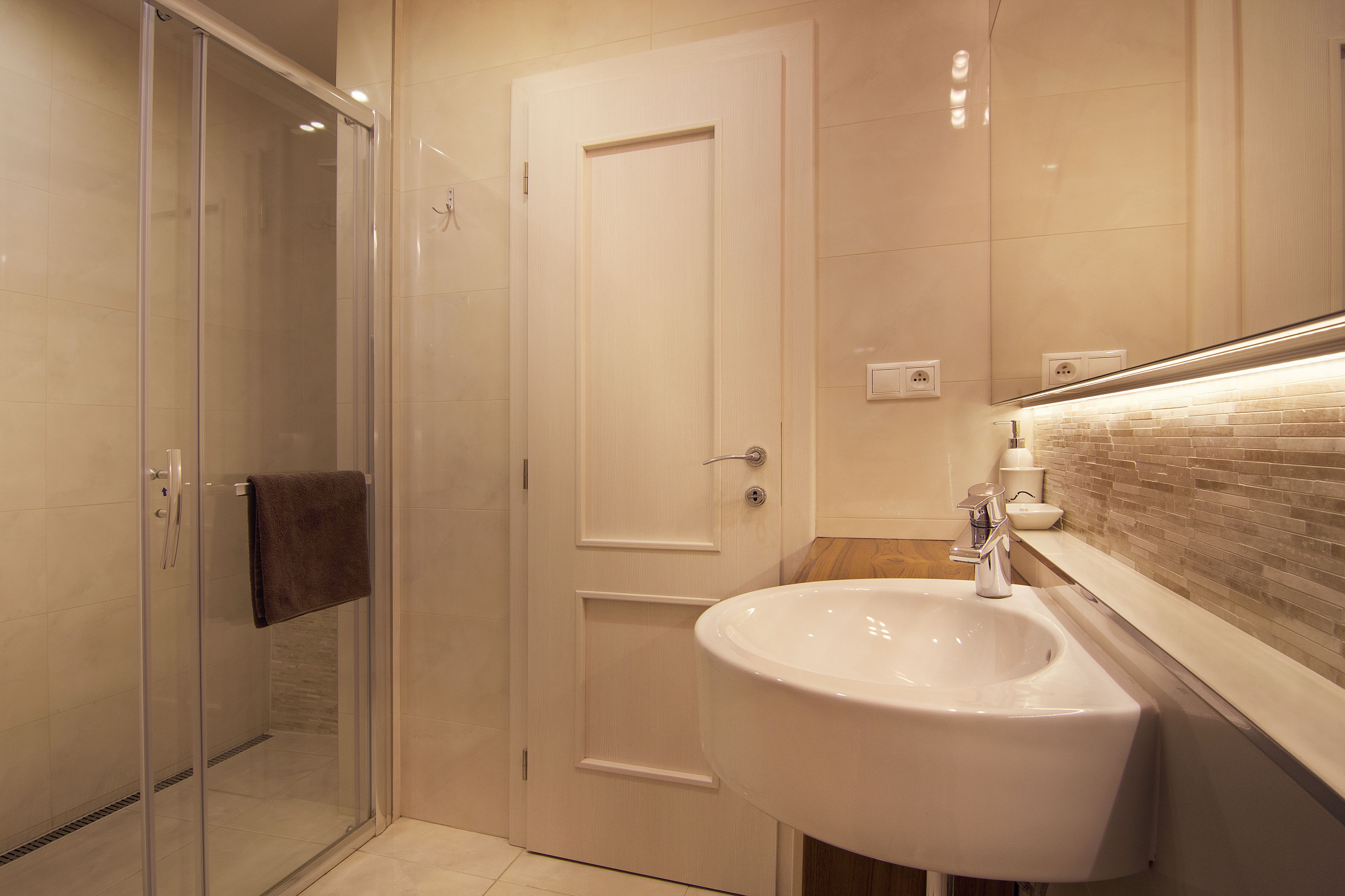 A modern bathroom with a glass shower enclosure, a white sink, and a tiled backsplash.