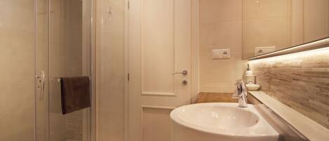Un baño moderno con cabina de ducha de vidrio, un lavabo blanco y un salpicadero de azulejos.