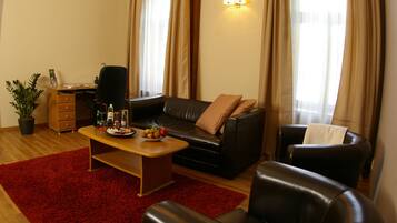A living room with a black leather sofa, a wooden coffee table, and a red rug. There is a desk with a chair and a potted plant.