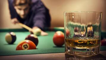 A billiards table with balls and a glass of whiskey.