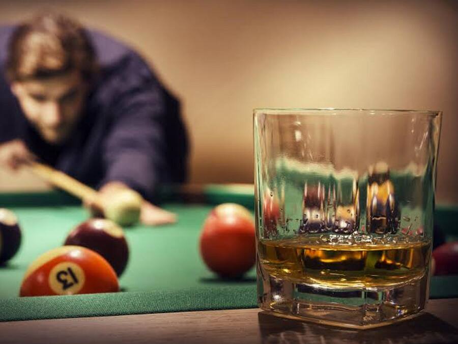 A billiards table with balls and a glass of whiskey.