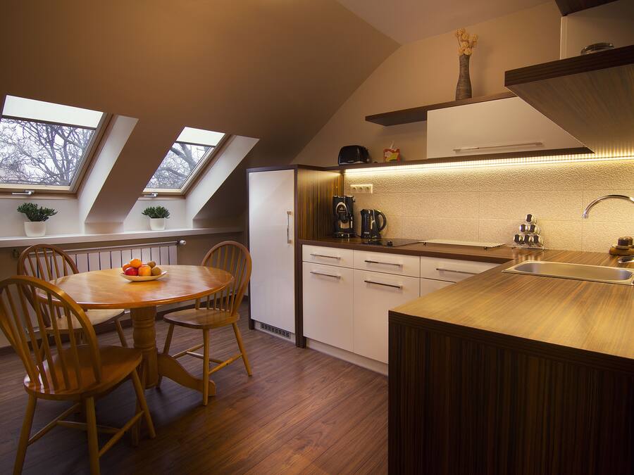 Eine moderne Küche mit Oberlichtern, einem Essbereich mit Holzstühlen und einer integrierten Kochinsel mit Spüle.