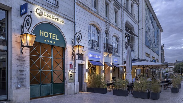 Un hotel con una amplia entrada arqueada, zona de estar al aire libre y un restaurante contiguo.