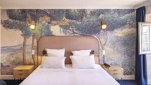 Habitación de hotel con cama, dos mesitas de noche, teléfono y un mural en la pared con motivos naturales.